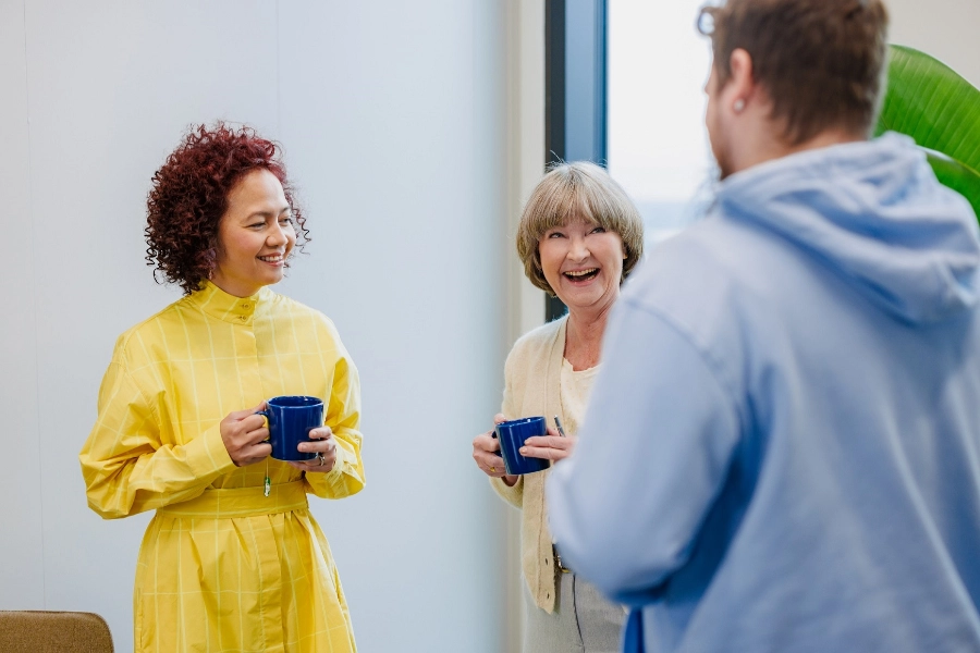 Two women and a man talking with coffee mug in hands
