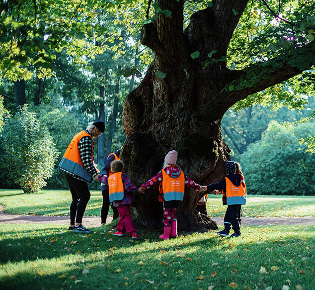 Children in bright orange vests circling a tree.