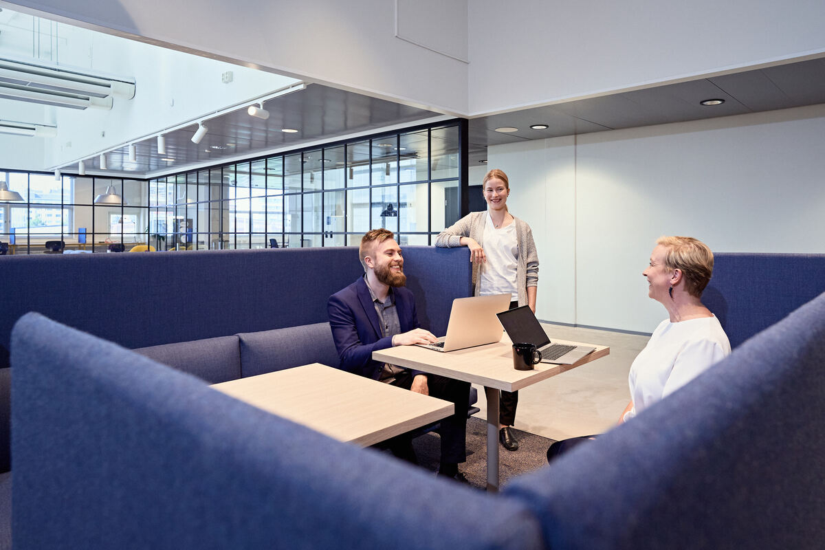 Colleagues meet with their laptops inside a modern office building.