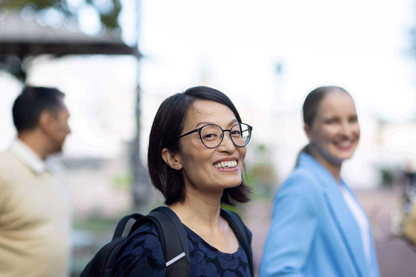 A woman smiling and looking at a camera with two persons on a background