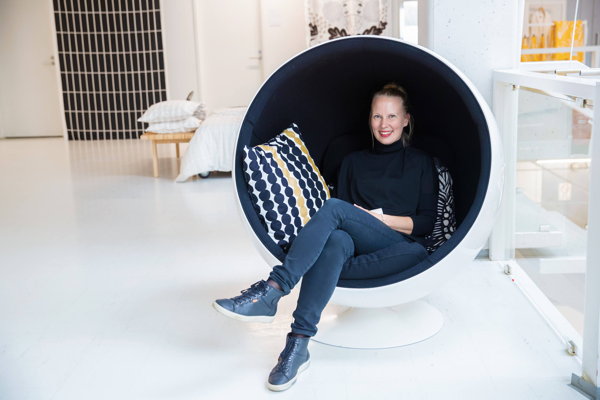 A woman wearing jeans sits inside a modern egg-shaped chair.