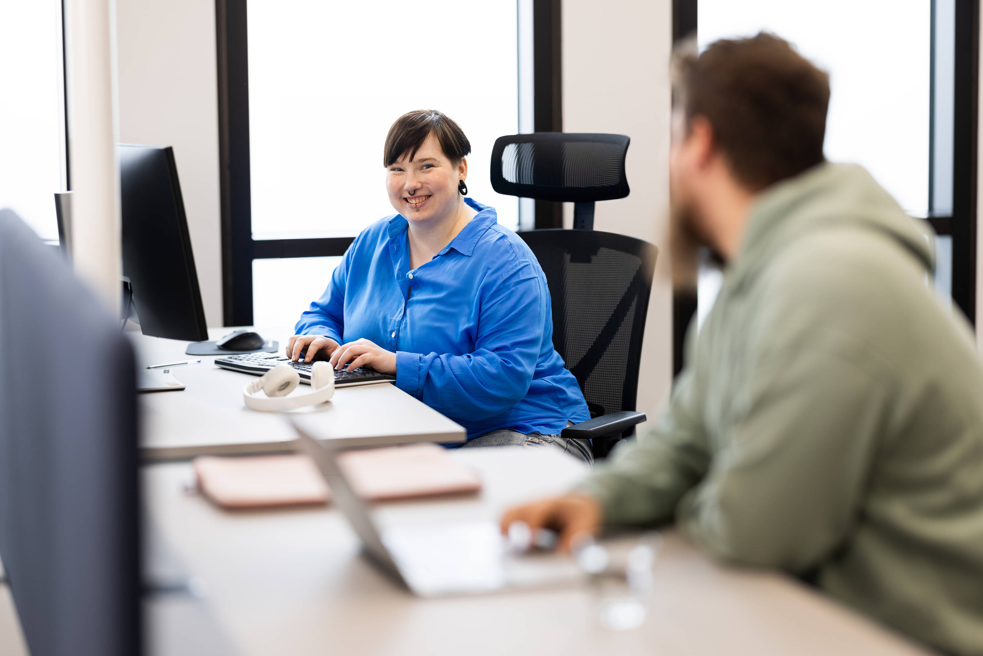 Two person at an open office working and  smiling  - Markus Pentikäinen / Keksi